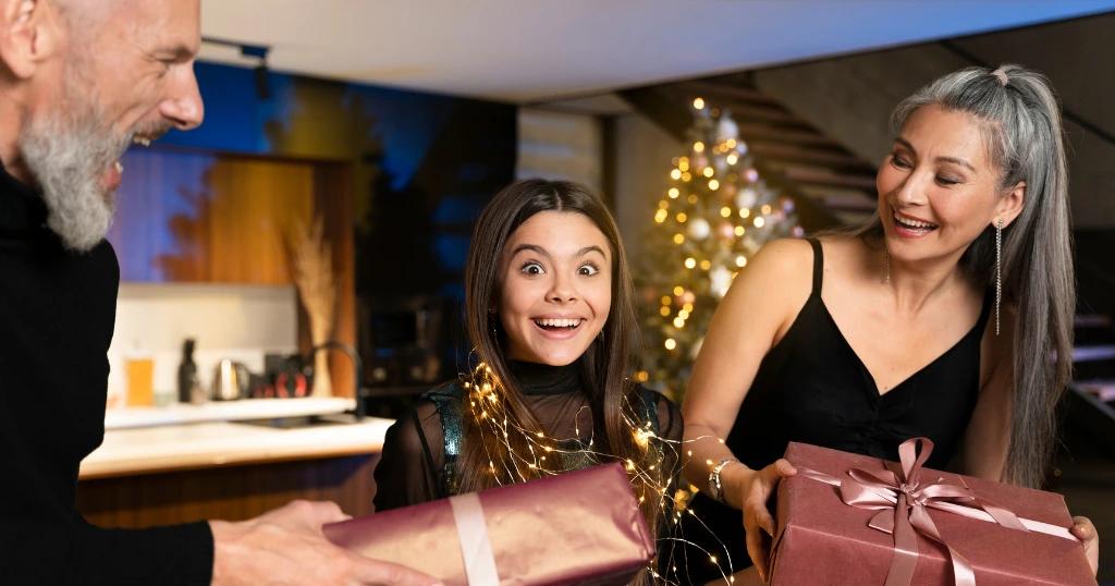 Excited family exchanging Festive Corporate Gifts during a holiday celebration by a Christmas tree, with lights and decorations in the background.