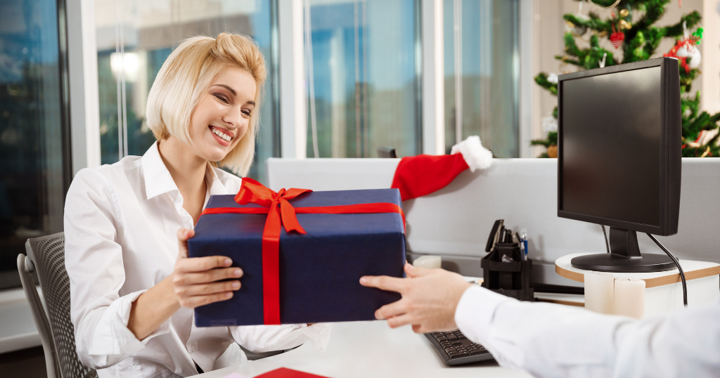 A blonde businesswoman happily receiving a luxury corporate gift in a festive office setting, highlighting premium corporate gifts during the holiday season in Dubai.