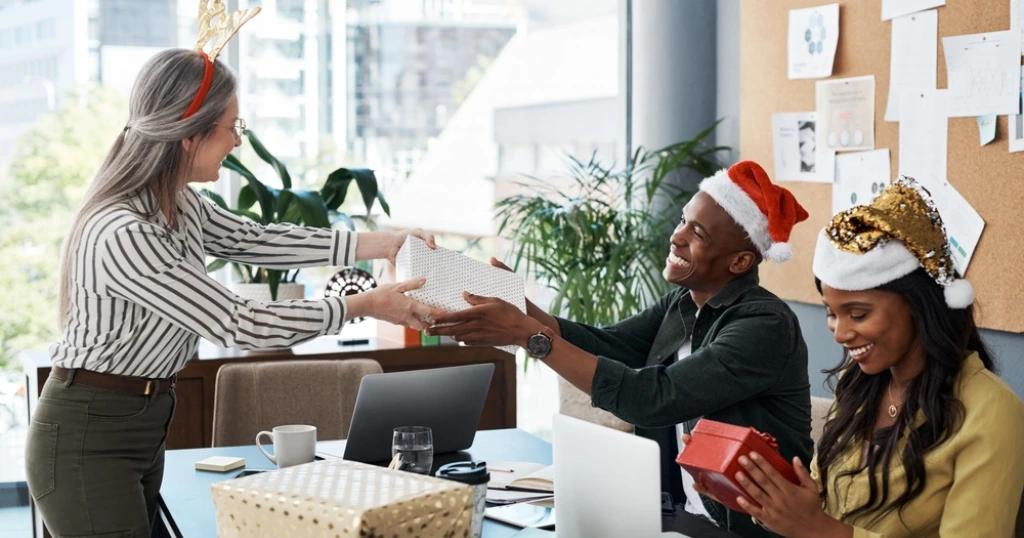 Happy employees sharing holiday gifts in a modern office – make the season special with Festive Corporate Gifts.