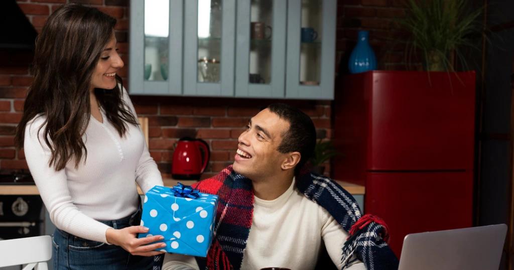 A woman presenting a blue promotional gift in Dubai to a delighted man in a modern kitchen.