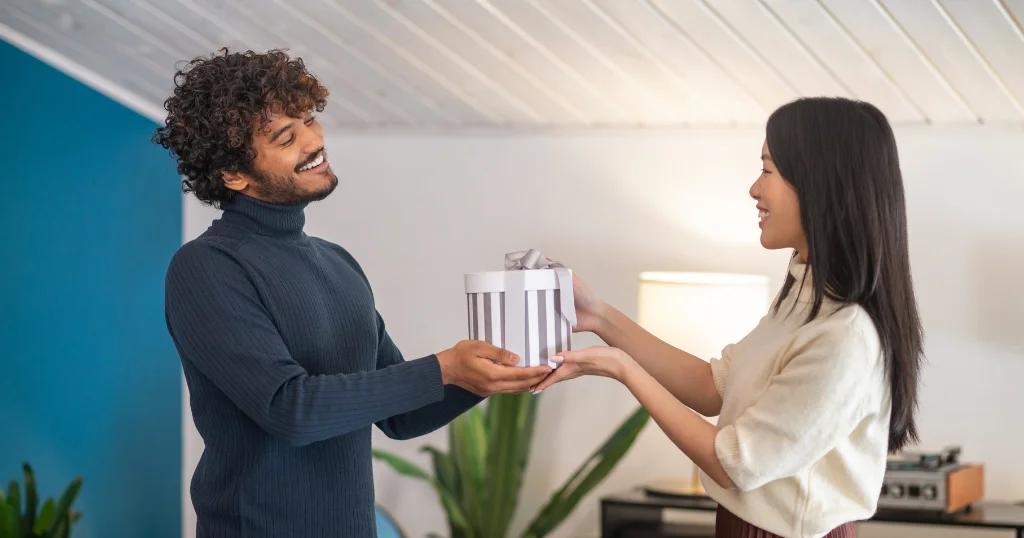 A man happily giving a gift to a woman at home, representing corporate gifting for remote employees in the UK.